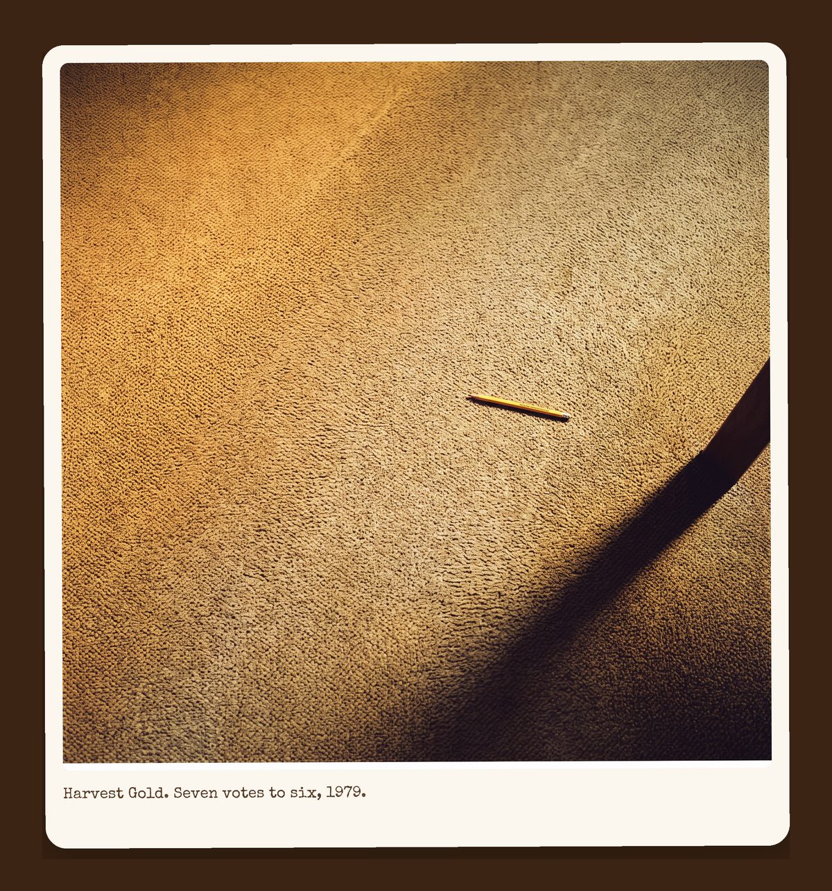 Harvest Gold carpet filling the frame, worn to a lighter traffic lane down the center, one dropped attendance pencil.